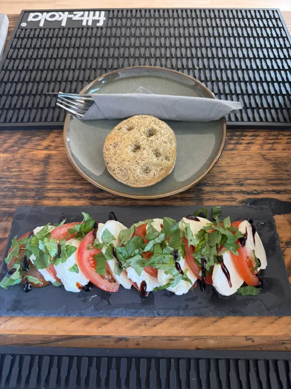 Tomate-Mozzarella-Platte mit Basilikum und Balsamico-Creme, dazu ein Focaccia-Brötchen