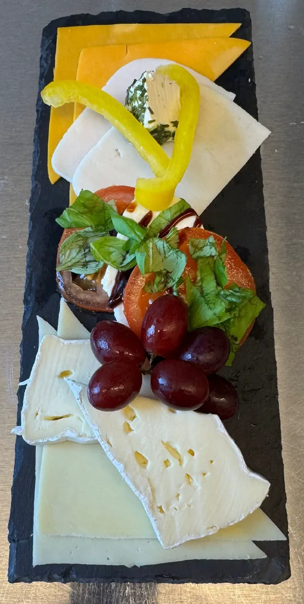 Käseplatte mit verschiedenen Käsesorten, Trauben und Basilikum-Tomate-Deko auf Schieferbrett
